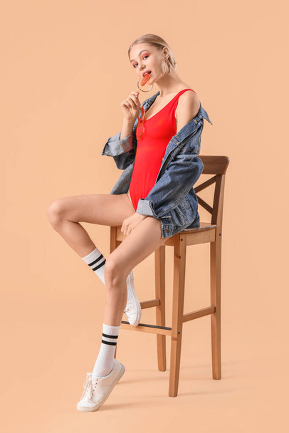Beautiful fashionable woman sitting on chair against color background - Photo, Image