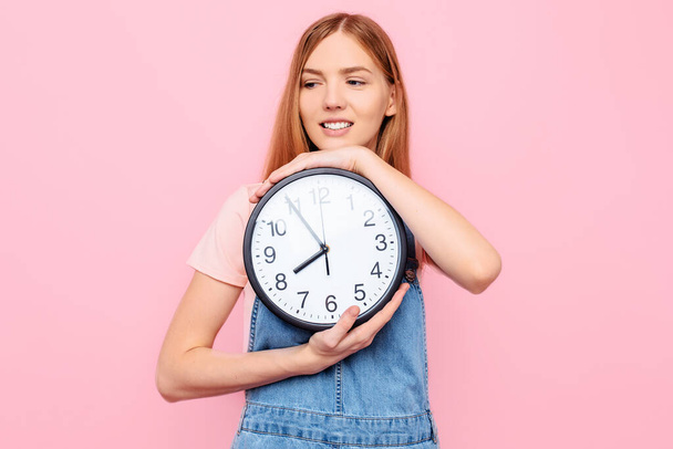 Happy smiling young girl with a watch in her hands, on an isolated pink background - Foto, Imagem
