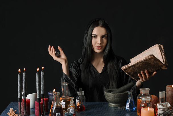 Alchimiste féminine faisant de la potion sur fond sombre - Photo, image