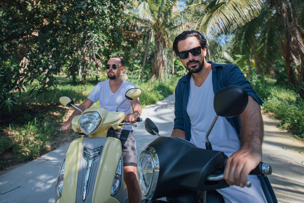 Двое мужчин на мотоциклах в пальмах на тропическом острове. Ребята туристы на велосипедах по дороге в пальмовой роще
 - Фото, изображение