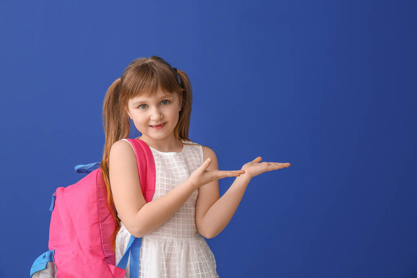 Roztomilé malá školačka ukazuje něco na barevném pozadí - Fotografie, Obrázek