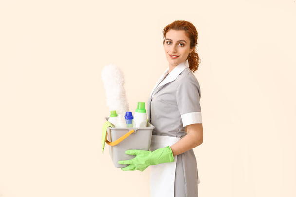 Beautiful young chambermaid with cleaning supplies on color background - Photo, Image