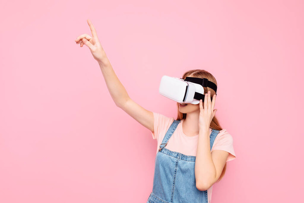 Young beautiful stylish woman with virtual reality glasses, on an isolated pink background - 写真・画像