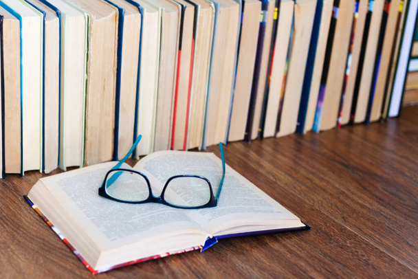 Open textbook, glasses, stack of old book on wooden table, education concept background, many books piles with copy space for text - Fotoğraf, Görsel