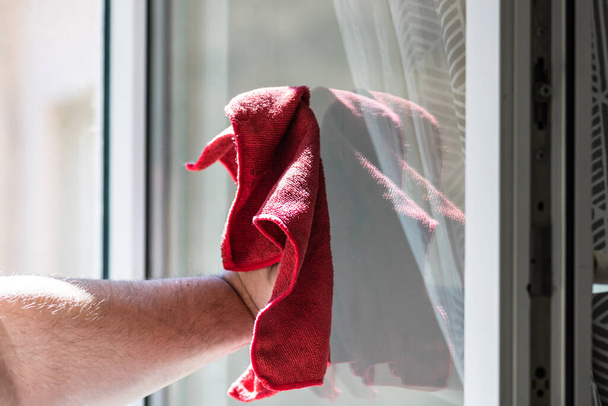 Mann wischt Fenster mit rotem Mikrofaserteppich ab, Reinigungsdienstkonzept. Hauswirtschaftskonzept - Foto, Bild