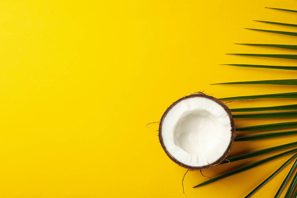 Half of coconut and palm leaf on yellow background, top view - 写真・画像