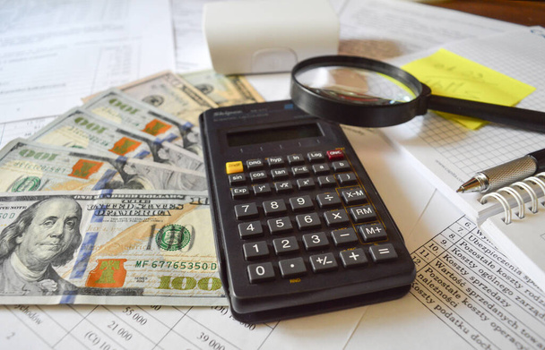 Lupa, kalkulačka, peníze a pero leží na dokumentech. Kancelářské potřeby jsou na finančních výkazech - Fotografie, Obrázek