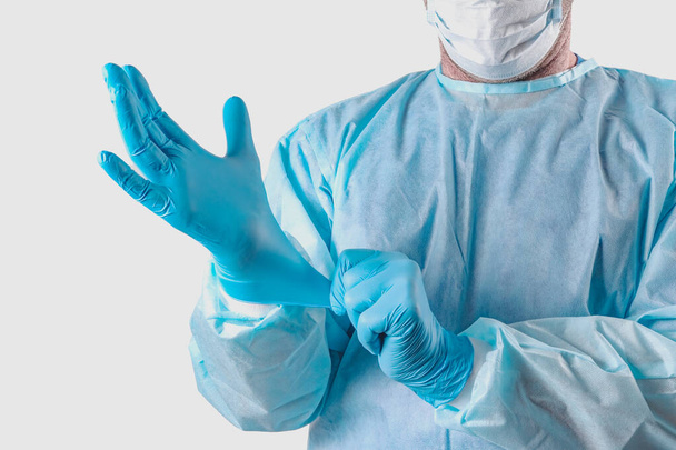 A medic in a protective suit puts on medical gloves. Personal protection for the coronavirus pandemic infection virus covid 19. Protective medical equipment for laboratories, research hospitals - Foto, Imagem