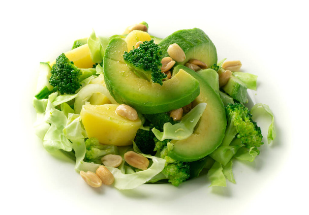 Zöld saláta avokádóval, uborkával, brokkolival, burgonyával és mogyoróval, fehér éttermi tányéron. Egészséges vegetáriánus saláta szeletelt aligátorkörtével vagy avokádós körtével - Fotó, kép