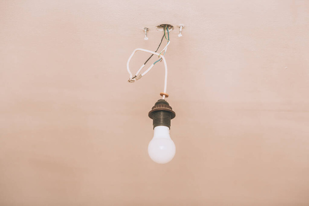 Лампочка на потолке. Одинокая лампочка и проволока торчат из потолка во время ремонта. - Фото, изображение