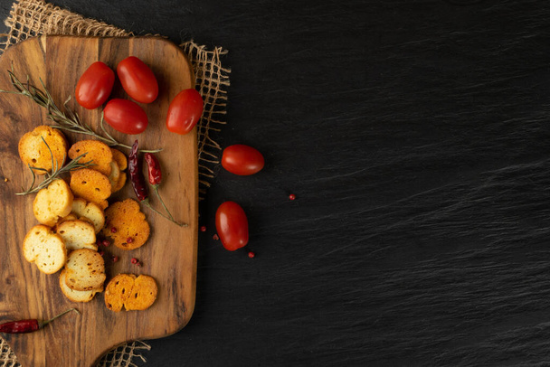 Homemade hot crunchy croutons in rustic style on wooden cutting board. Round spicy bruschetta crackers, seasoning rusks or small fried bread snacks with copy space - Photo, image