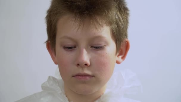 Χαριτωμένο παιδί με προστατευτική στολή που φοράει ιατρική μάσκα προσώπου κατά τη διάρκεια του ιού του στέμματος του στέμματος και της γρίπης σε φόντο λευκού τοιχώματος από κοντά. Έννοια προστασίας ιών Covid-19. Κατάσταση έκτακτης ανάγκης. - Πλάνα, βίντεο