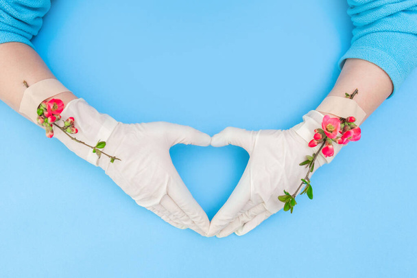 Весенние розовые цветы с клейким пластырем на руке с белой медицинской перчаткой, на голубом фоне. Концепция прекращения болезни или пандемии
. - Фото, изображение