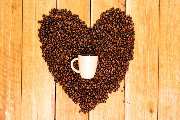 Une tasse de café et des grains de café frits sous la forme d'un cœur sur un fond en bois noir
 - Photo, image