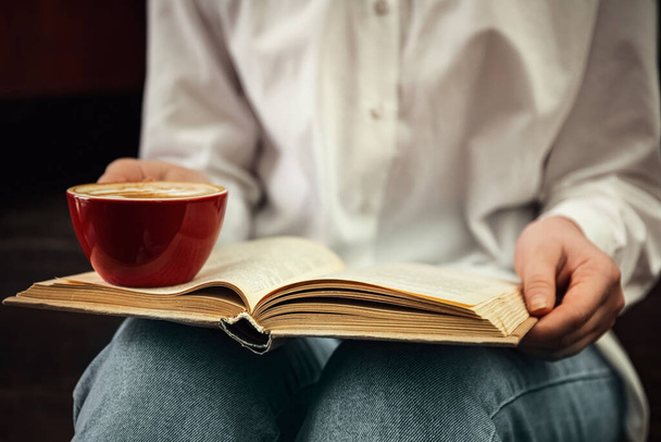 Woman with cup of coffee reading book indoors, closeup - Foto, afbeelding