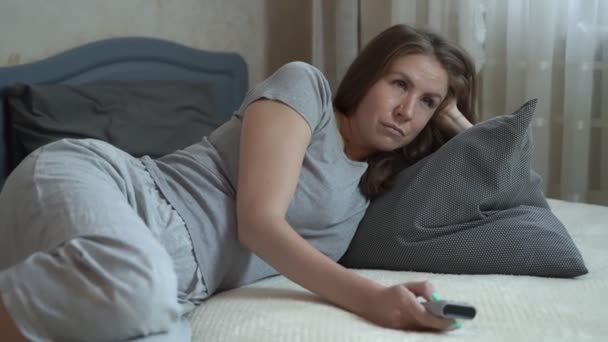The girl lies on the bed in a small room and watches a small TV - Záběry, video