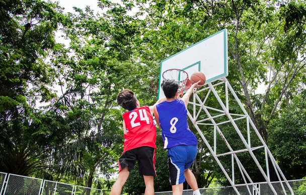 achtertuin van basketbalspeler die bal speelt. Schieten om doel mand in groene boom outdoor court - Foto, afbeelding