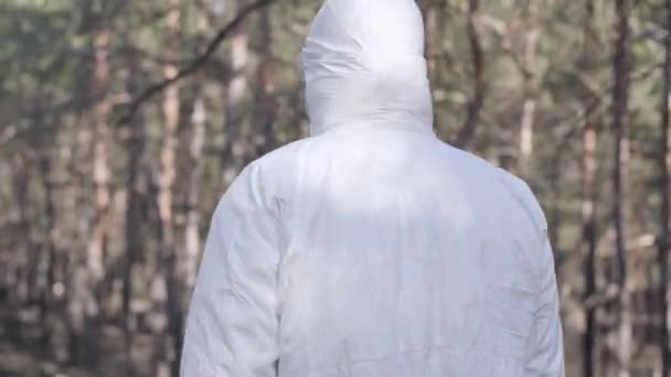 Unknown man in white protective suit walking in spring forest or park on sunny day. Guy spending coronavirus quarantine outdoors following WHO safety recommendations. Covid-19, pandemic, danger. - Πλάνα, βίντεο