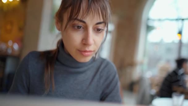 Νεαρή γυναίκα που επικεντρώνεται στην οθόνη και δακτυλογράφηση σε φορητό υπολογιστή, ενώ κάθεται στο γραφείο στο χώρο εργασίας ή καφέ. - Πλάνα, βίντεο