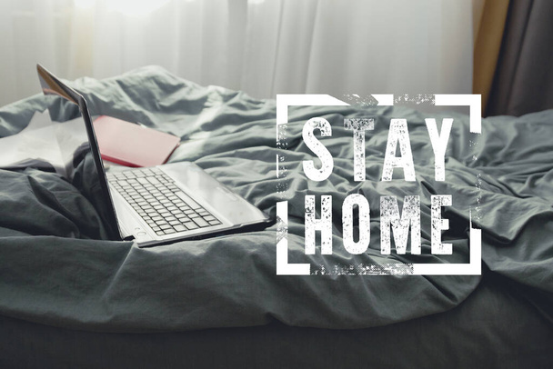 Práce doma, práce na dálku. Notebook s poznámkovým blokem na posteli v pokoji a nápisem Zůstaňte doma - Fotografie, Obrázek