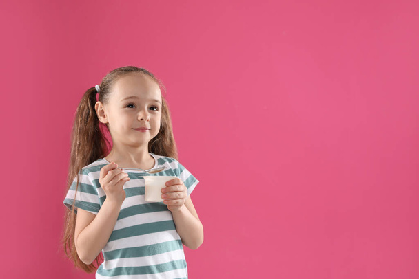 Cute little girl with tasty yogurt on pink background. Space for text - Foto, afbeelding
