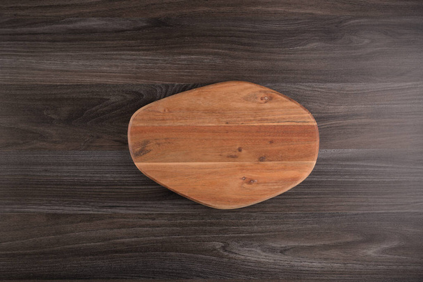 Top view of wooden cutting board on old dark wood countertop. - Foto, afbeelding