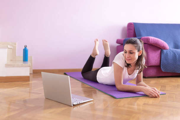 Szczęśliwa młoda biała kobieta, ogląda zajęcia na laptopie w salonie. Opieka zdrowotna i wellness w domu. - Zdjęcie, obraz