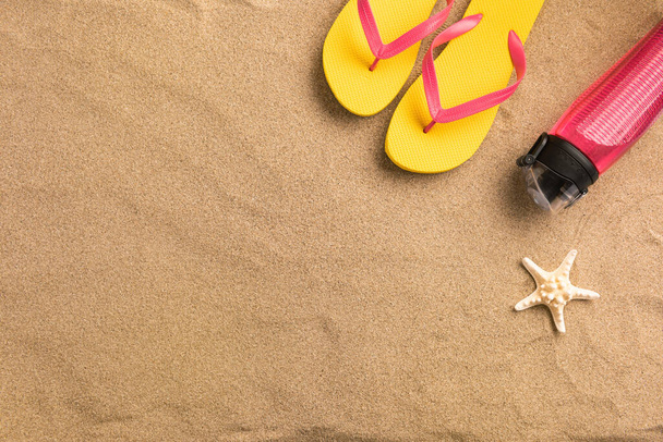 Summer fashion, summer outfit on sand background. Yellow flip flops and bottle of water. Flat lay, top view - Foto, Imagem