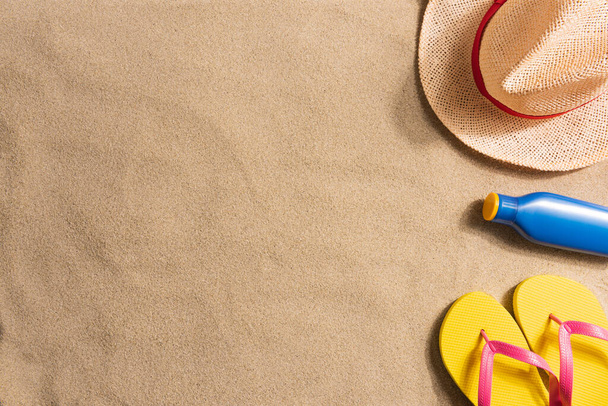 Summer vacation composition. Sun cream, flip flops and straw hat on sand  - Fotografie, Obrázek