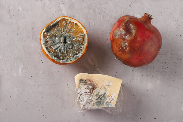 Zepsute zgniłe jedzenie z pleśnią: pół pomarańczy, granat i twardy ser na szarym tle, widok z góry - Zdjęcie, obraz