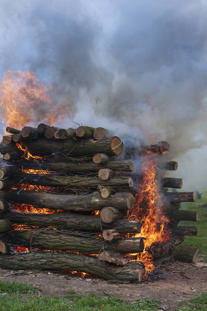 Hölzerne Einfassung auf einer Wiese, die während der Hexenverbrennung als Kamin angezündet wird. Feuer, Rauch und heiße Kohlen sind zu sehen. - Foto, Bild
