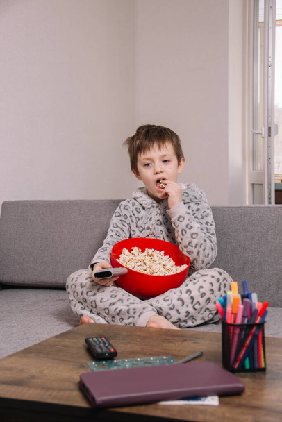 Mies istuu sohvalla ja syö popcornia eristyksissä katsoessaan elokuvaa tai sarjakuvaa.
 - Valokuva, kuva