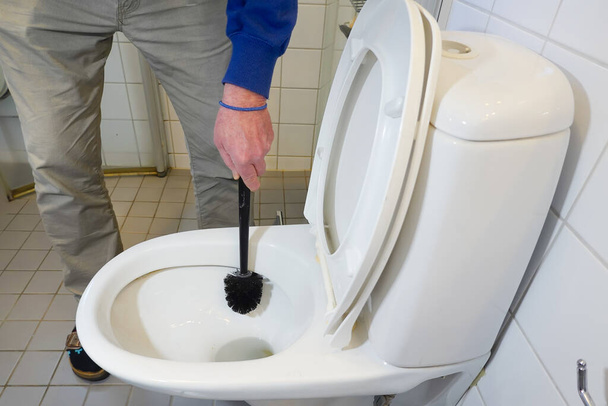 Een man poetst een toilet schoon in een appartement - Foto, afbeelding