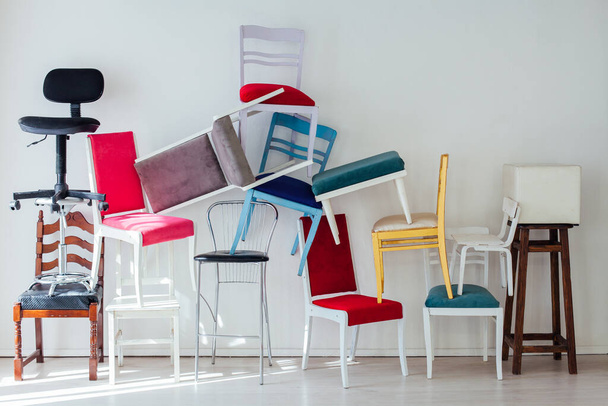 πολλές πολύχρωμες καρέκλες στέκονται στον τοίχο του εσωτερικού του λευκού δωματίου - Φωτογραφία, εικόνα