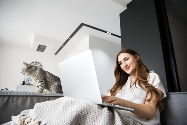 Happy young Girl Works at Home with a Computer with a Cat - Photo, image