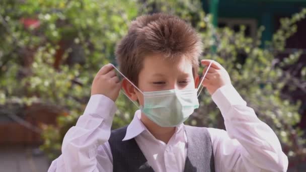 Young attractive Caucasian kid in school suit takes off protective medical mask, inhales and enjoys clean air during quarantine slow motion. Covid 19 virus healing concept. Sunny day in the garden. - Footage, Video