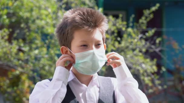 Little boy in white shirt and gray vest takes off protective medical mask from his face, enjoying wonderful morning air on sunny day slow motion. Man does not afraid coronavirus covid-19 virus threat. - Filmati, video