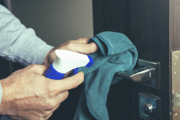 closeup of a caucasian man disinfecting the door handle by spraying a blue sanitizer from a bottle - Foto, afbeelding