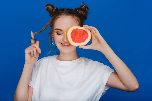 Surprised, the laughing girl holds the grapefruit like ears. Vegan lifestyle. Smiling woman , eating concept.Diet organic , weight loss and healthy food. Smoothies and fresh juice. - Foto, afbeelding