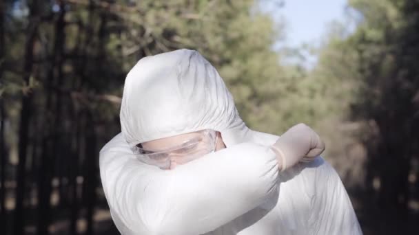 Portrait of young man in safety suit sneezing or coughing and showing thumb up. Caucasian virologist wearing face mask outdoors on Covid-19 quarantine. Coronavirus symptoms, infectious disease. - Filmati, video