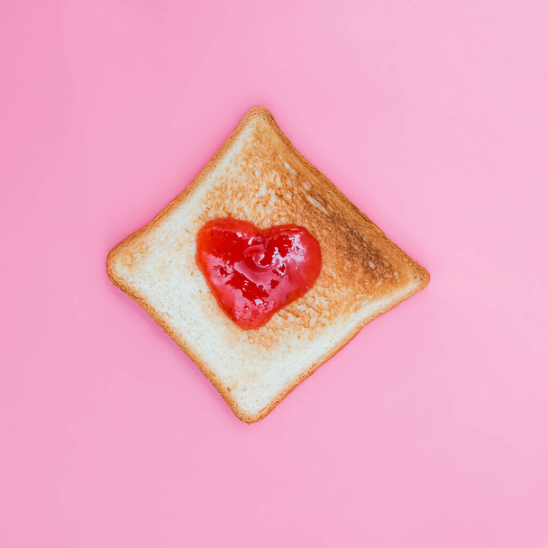 Toasted bread with strawberry jam in heart shape on pink background - Fotoğraf, Görsel