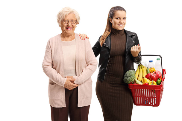 Young woman helping an elderly lady with a shopping basket posing isolated on white background - Foto, Bild
