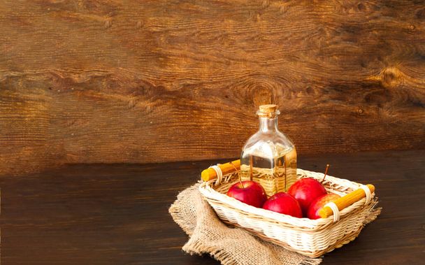 Appelciderazijn in glazen fles en rode appels op houten ondergrond. Close-up, kopieerruimte - Foto, afbeelding
