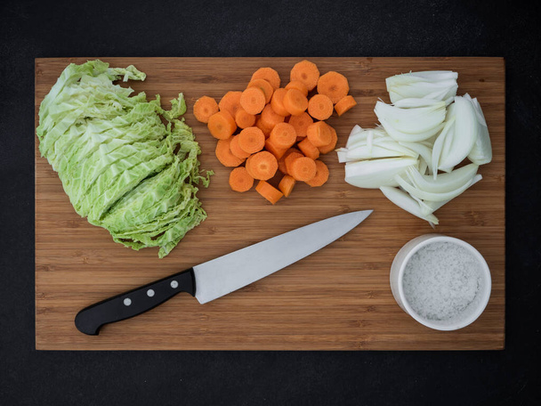 Col, cebolla, zanahorias y cuchillo de cocina en la tabla de cortar madera. vista superior - Foto, imagen