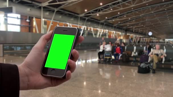Mão masculina segurando um Smartphone antigo no Hall de um aeroporto com pessoas desfocadas no fundo. Você pode substituir a tela verde com a filmagem ou imagem que você deseja com efeito Keying em After Effects (confira tutoriais no YouTube
).  - Filmagem, Vídeo