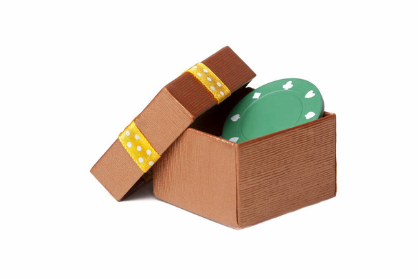 Une nouvelle puce de poker verte cachée dans une boîte cadeau ouverte en or avec un ruban jaune et un couvercle mis de côté. Jetons gratuits donner, donner de l'argent, jeu gratuit et l'encouragement des jeux concept général
 - Photo, image