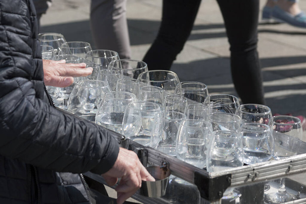 A busker, street performer, musician playing an unusual uncommon instrument made from wine glasses - glass harp. Concept of free street art performance and busking - Photo, Image