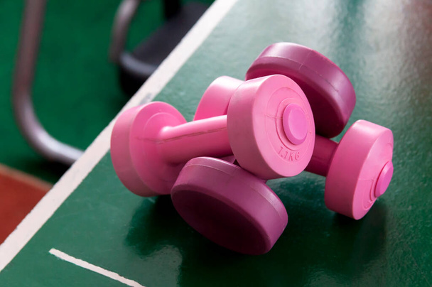 Two pink dumb bells laying on the table pong table. Feminine workout symbol, new female gym area heavy training and weight lifting equipment abstract, women's health concept, dumbbells on the table - Φωτογραφία, εικόνα