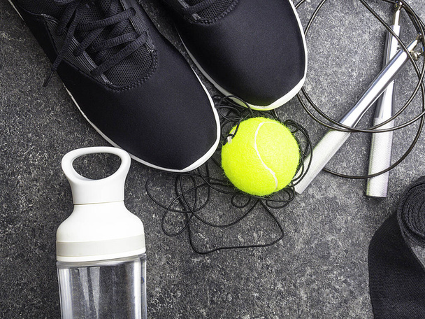 スポーツ用品、ブラックスニーカー、コンクリートの背景に、水のボトル、テニスボール、ジャンプロープ、ボクシングのための手の包帯と構成 - 写真・画像