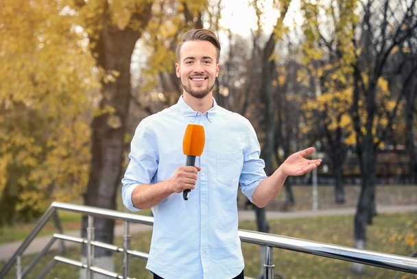 Jovem jornalista do sexo masculino com microfone trabalhando no parque
 - Foto, Imagem